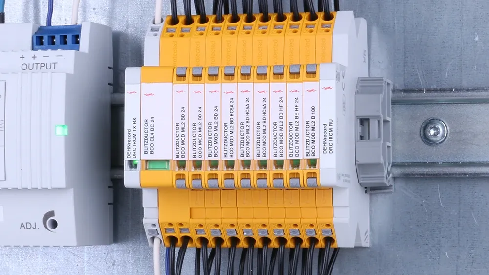Un descargador de sobretensiones amarillo y azul sobre una mesa delante de un armario eléctrico en segundo plano.