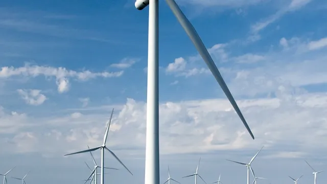 We see an offshore wind farm on the sea in slightly cloudy weather, with a wind turbine present in the foreground and many more in the background.
