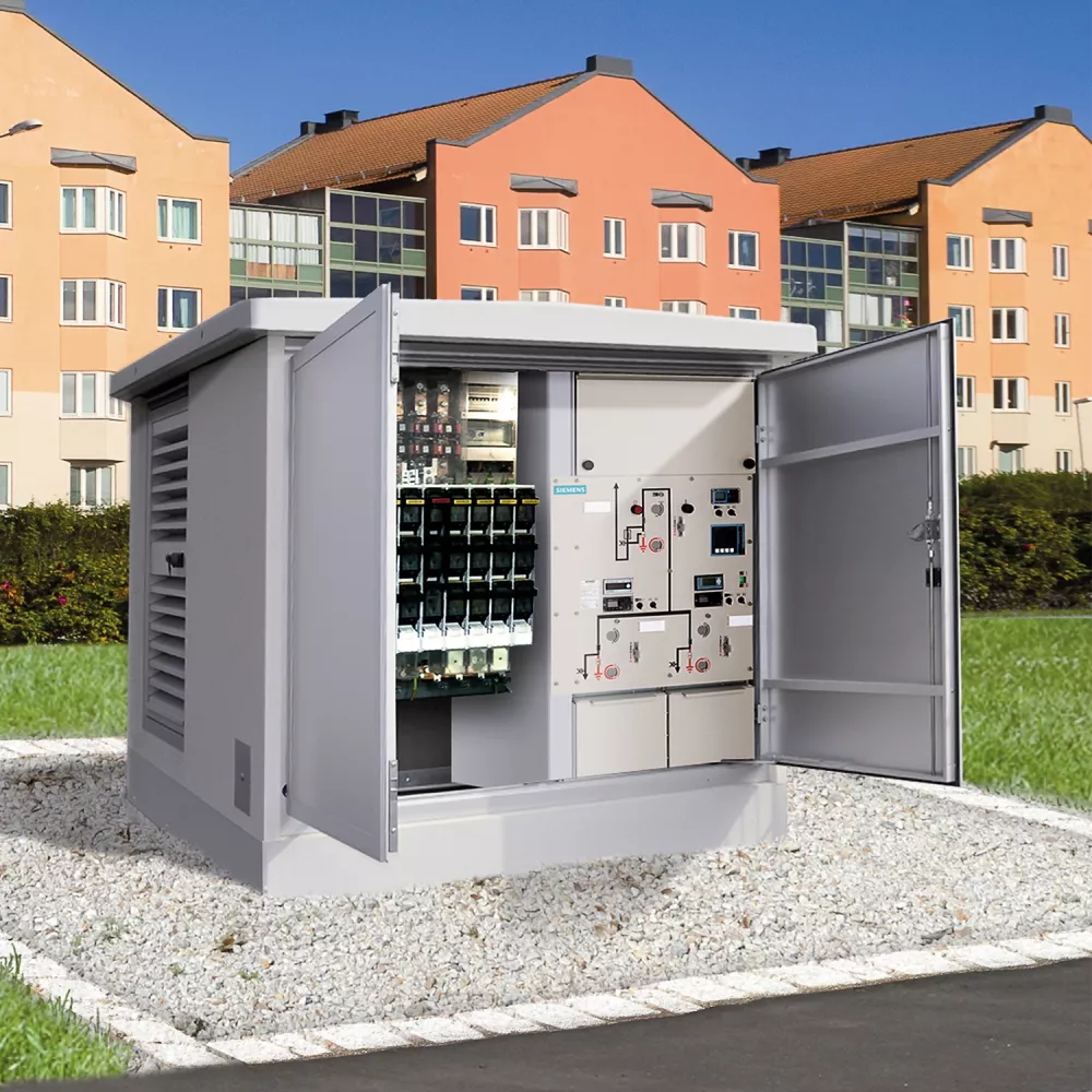 Outdoor electrical transformer station with open metal cabinet showing control panels, installed on gravel near residential buildings.