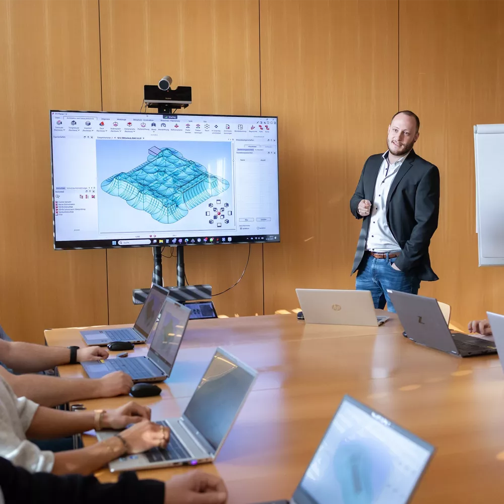 Training room with participants using laptops while a presenter explains a 3D electrical planning model on a large display.