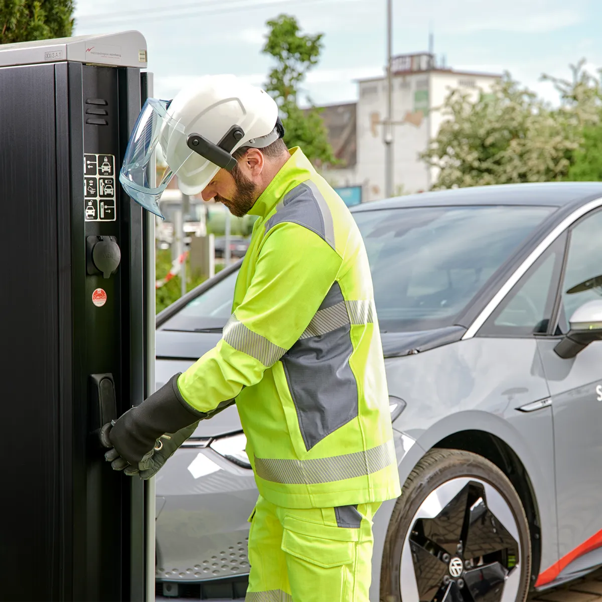 Person in safety vest and helmet connecting an electric vehicle to a charging station.