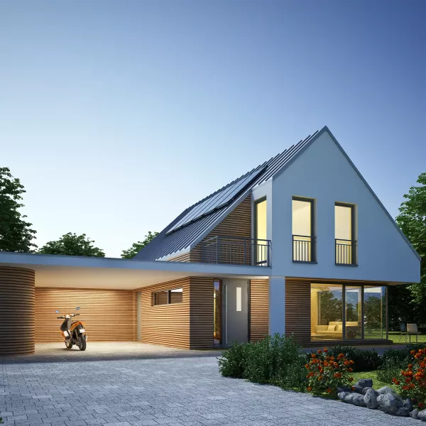 Modern detached house at dusk with solar panels on a pitched roof, illuminated windows, wooden facade elements, and a covered carport.
