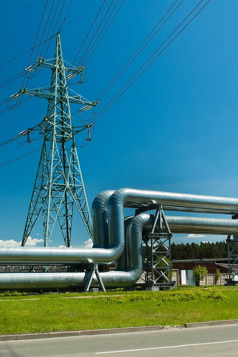 A captivating image displays a striking fusion, where a vibrant blue electrical tower stands tall against a contrasting silver gas pipe system. The low-angle perspective highlights the towers height and intricate pipe design, symbolizing the harmonious blend of modernity and tradition.