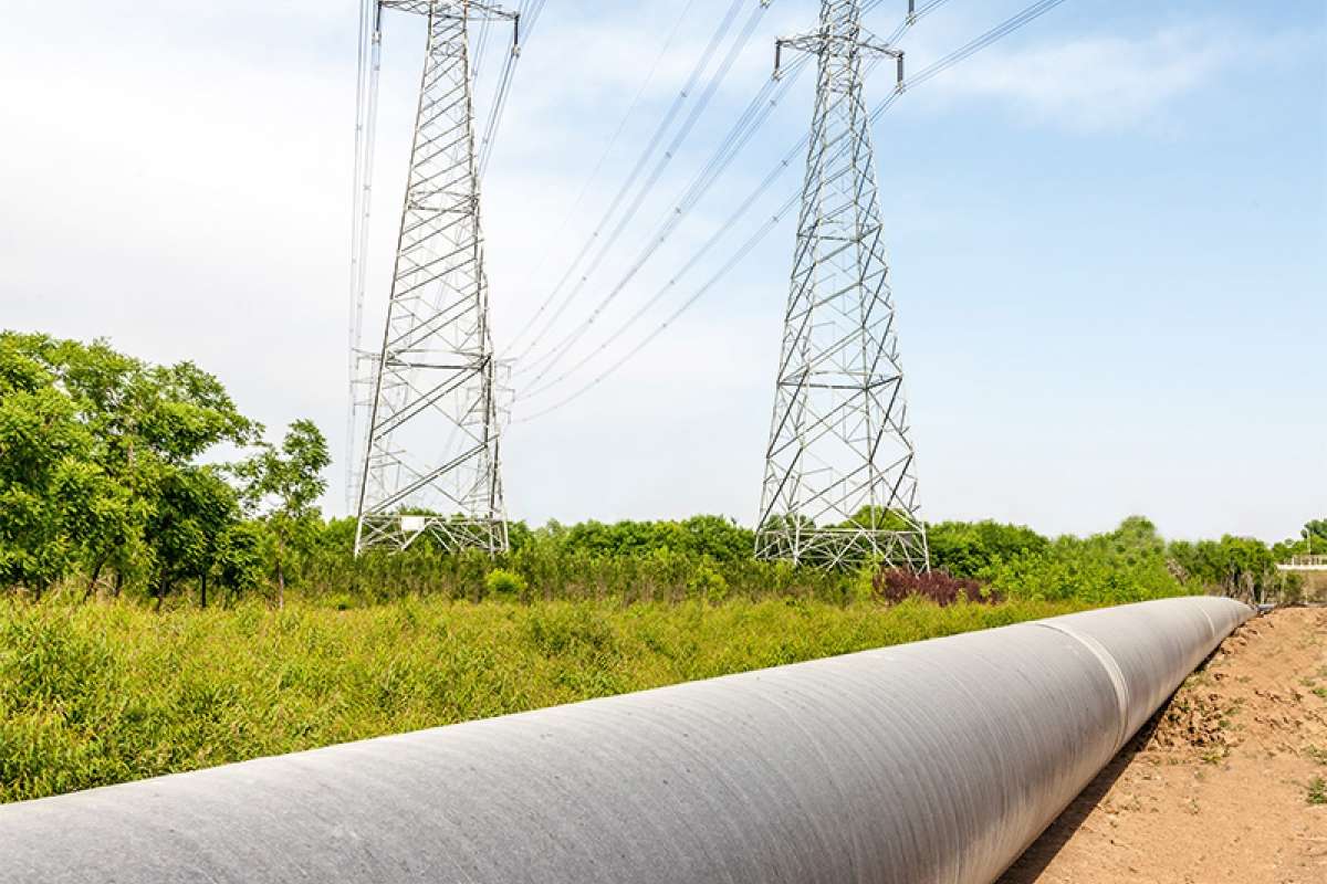 Línea de alta tensión y tubería sobre un prado verde delante de un bosque.