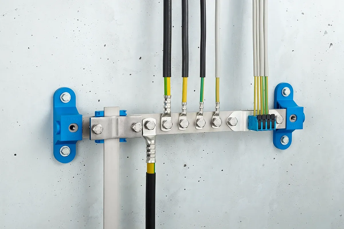 Barra de compensación de potencial con conexiones azules a la pared y cables negros, montada en una pared de hormigón gris.