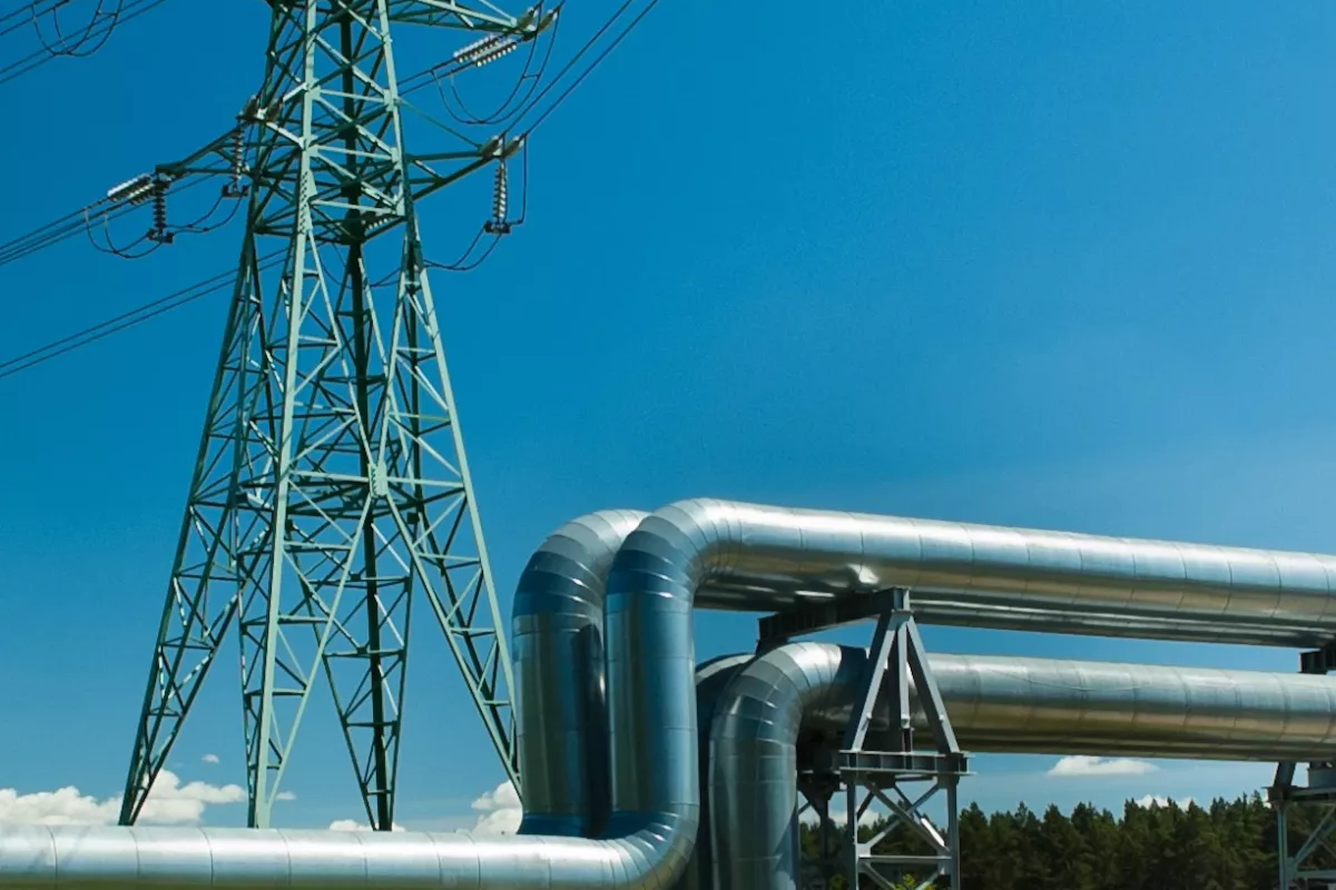 Línea de alta tensión y tubería sobre un prado verde ante un cielo azul.
